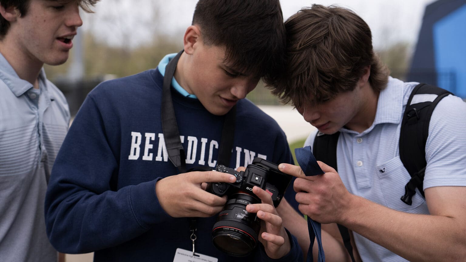 Three Benedictine students leaning in over a professional camera, one of them in a Benedictine crewneck working the controls while the other two read the shot on the screen.